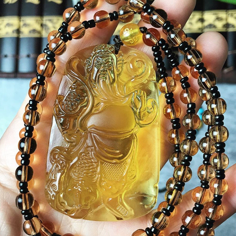 Hand holding a necklace with a clear pendant featuring an engraved design against a blurred background