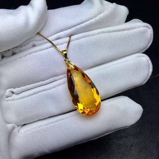 Yellow teardrop pendant held in a white gloved hand against a black background