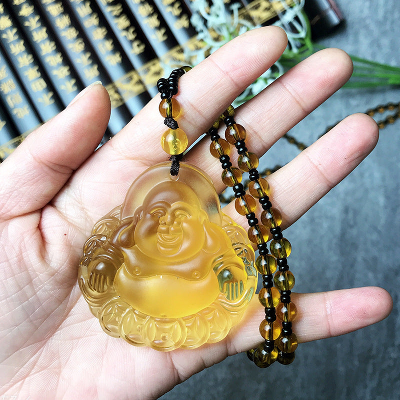 Hand holding a yellow Buddha pendant with a beaded chain against a blurred background