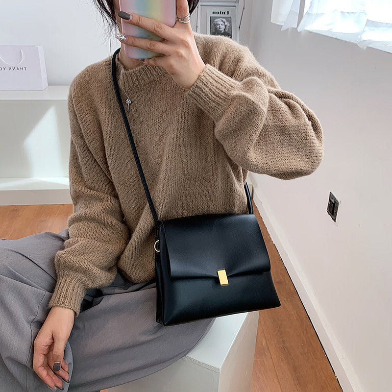Person wearing a brown sweater and holding a black handbag indoors.