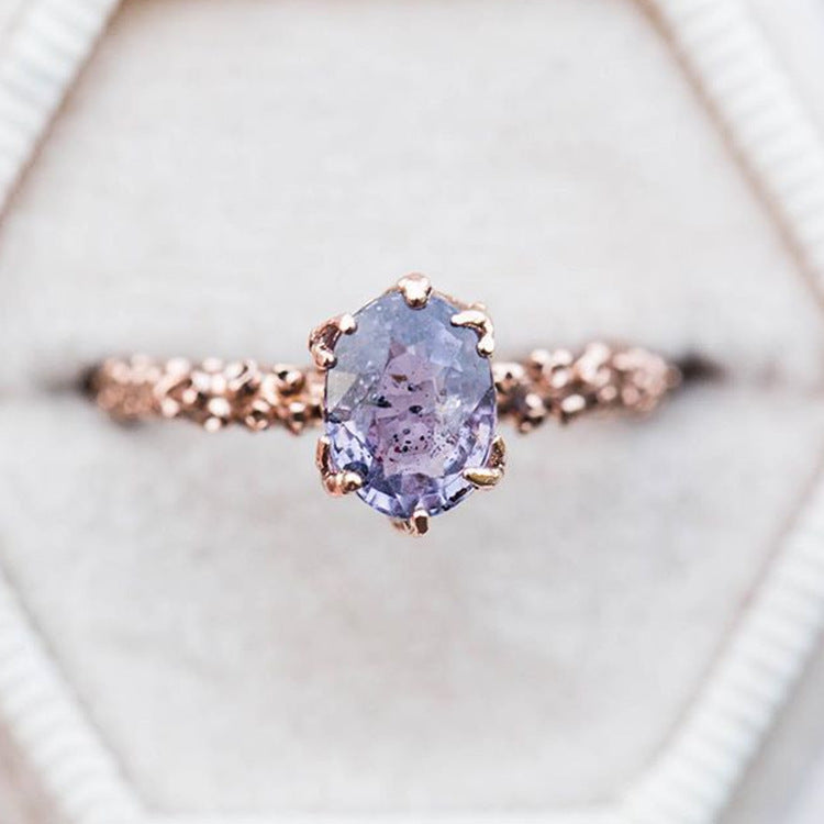 Rose gold ring with a purple gemstone on a light background
