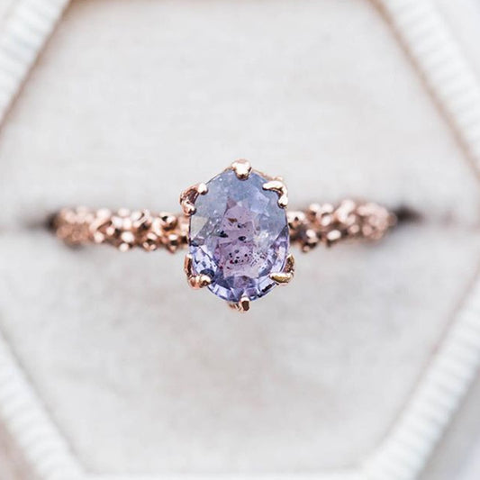 Rose gold ring with a purple gemstone on a light background