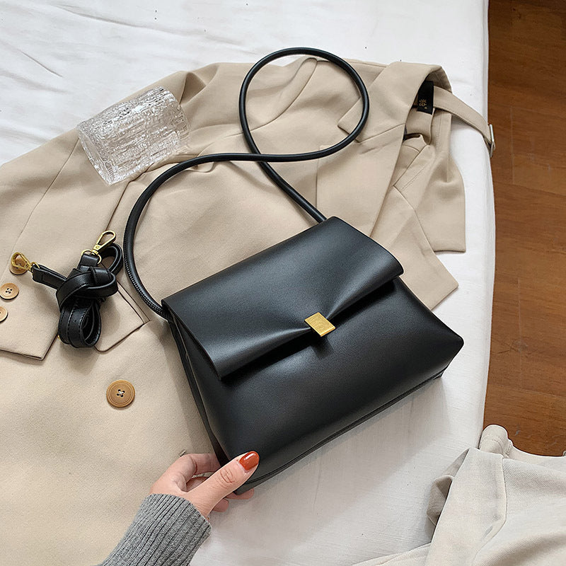 Black handbag held by a hand on a beige coat with a wooden floor background