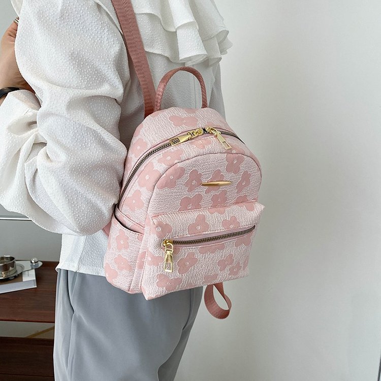 Person wearing a pink floral backpack with gold zippers against a neutral background