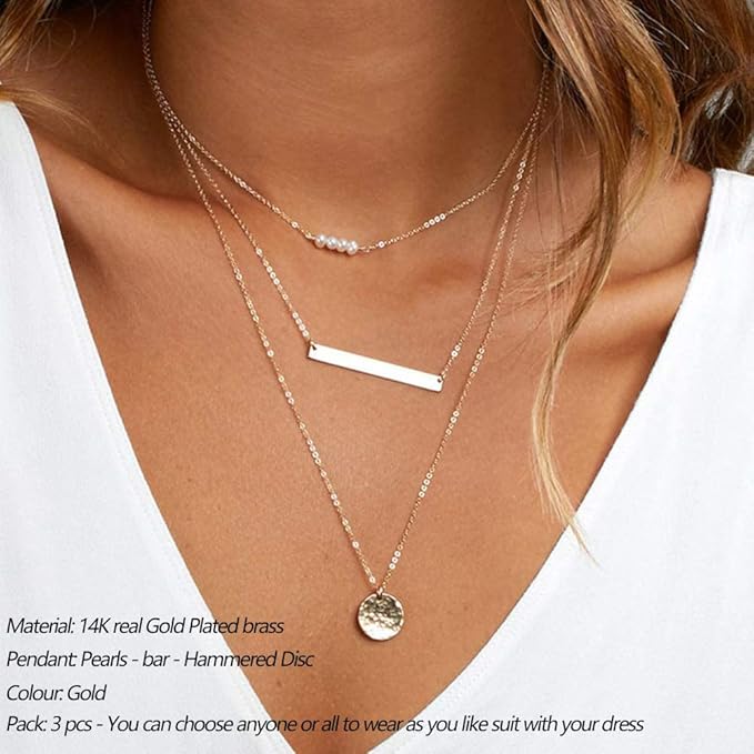 Gold necklaces with various pendants on a person wearing a white top.
