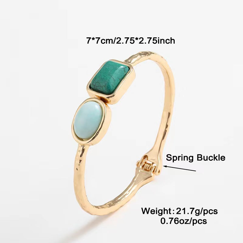 Gold bracelet with green and blue stones on a white background