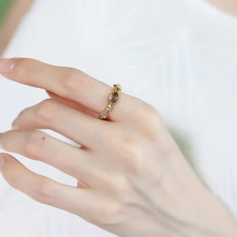 Hand wearing a ring with a green gemstone on a white background
