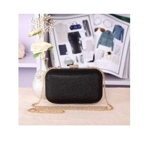 Black clutch bag with gold chain on a light surface with a magazine in the background