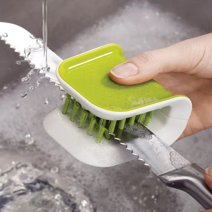 Green and white scrubber cleaning a knife under running water.