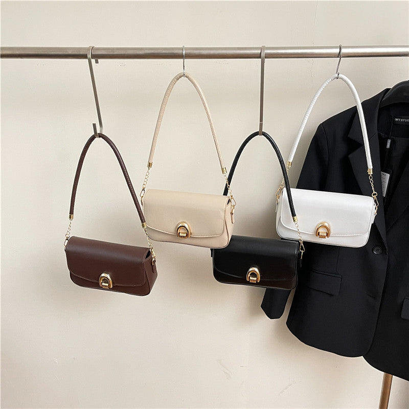 Four handbags in different colors hanging on a rack with a black blazer next to them.