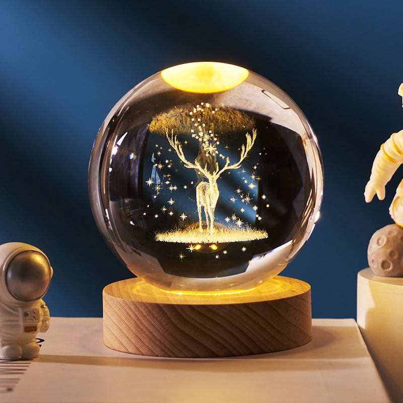 Decorative crystal ball with a tree and deer design on a wooden base, surrounded by small figurines.