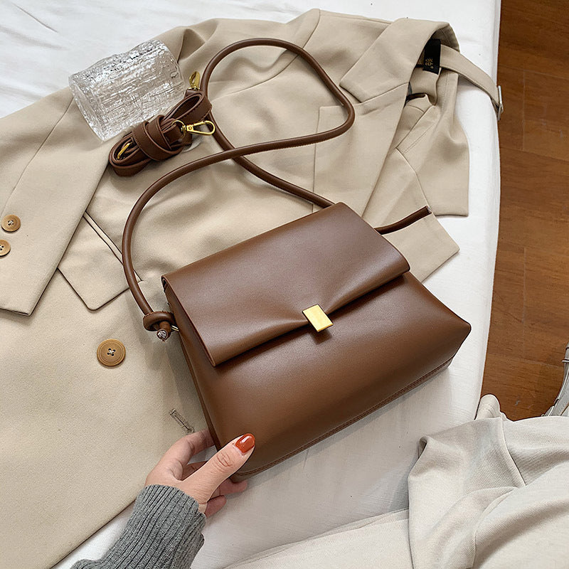 Brown handbag held by a hand with a beige coat and white surface in the background