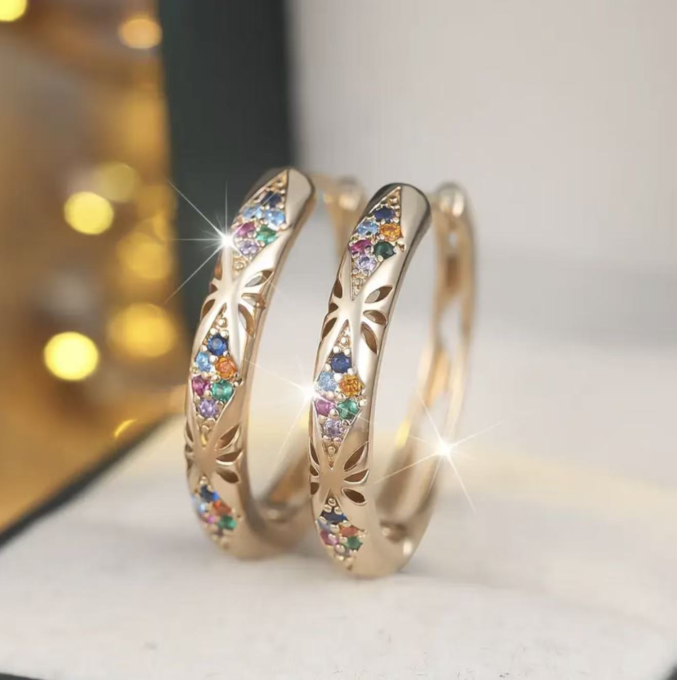 Gold hoop earrings with colorful gemstones on a white surface.