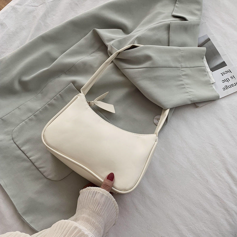 White handbag held by a hand on a light gray surface with a light gray jacket and newspaper in the background.
