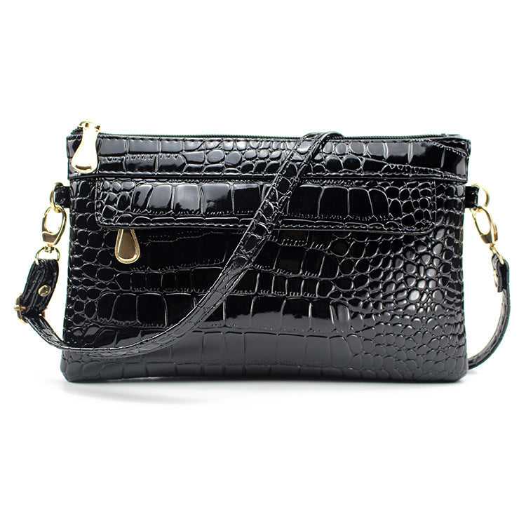 Black crocodile-patterned handbag with gold accents on a white background