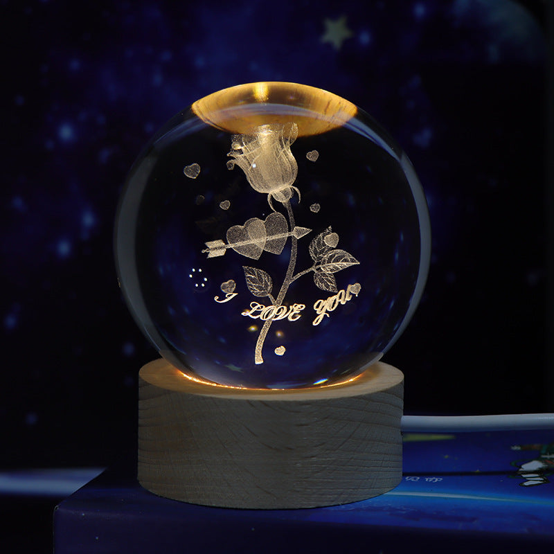 Decorative glass ball with floral design and 'I love you' text on a wooden base against a dark background.
