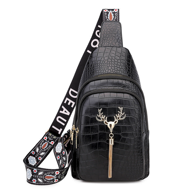Black crocodile-patterned sling bag with deer head tassel and decorative strap on a white background