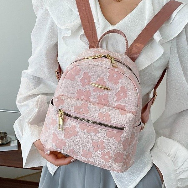 Person holding a pink floral backpack with a neutral background