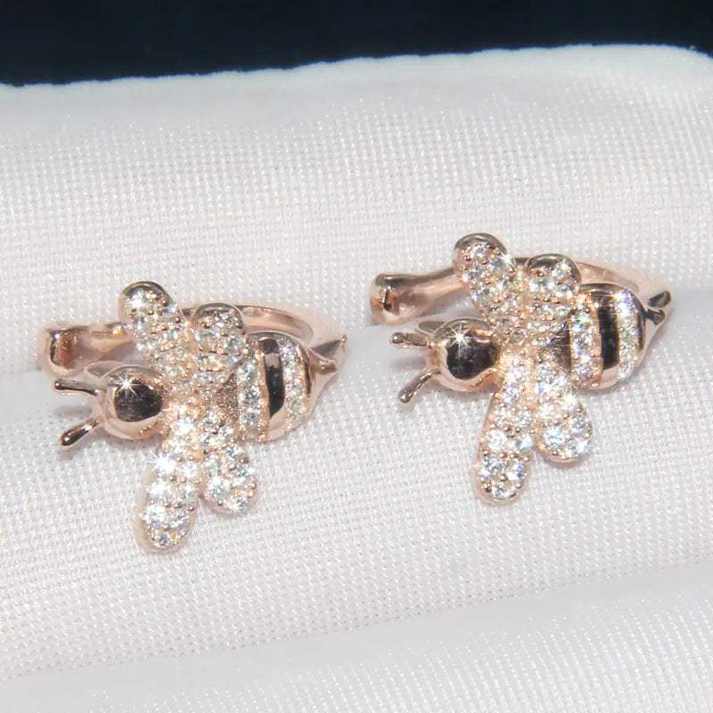 Rose gold bee-shaped earrings on a white cushion