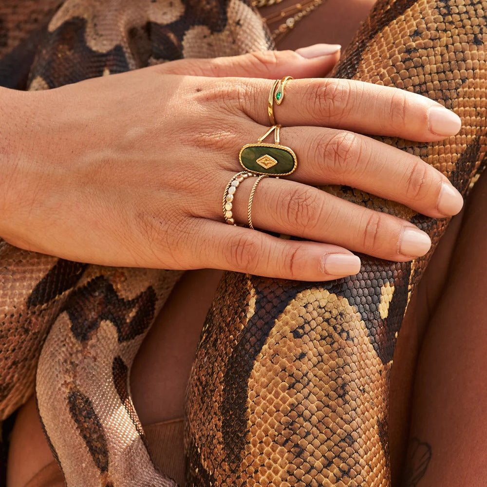 Close-up of a hand wearing gold rings with green gemstones on a snake skin background
