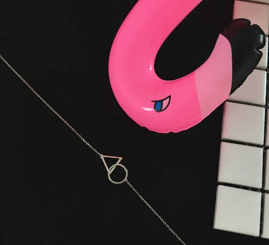 Pink flamingo pool float on a black surface with a necklace in the foreground