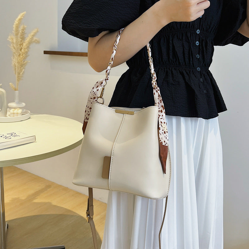 Person holding a beige handbag with a patterned strap in an indoor setting
