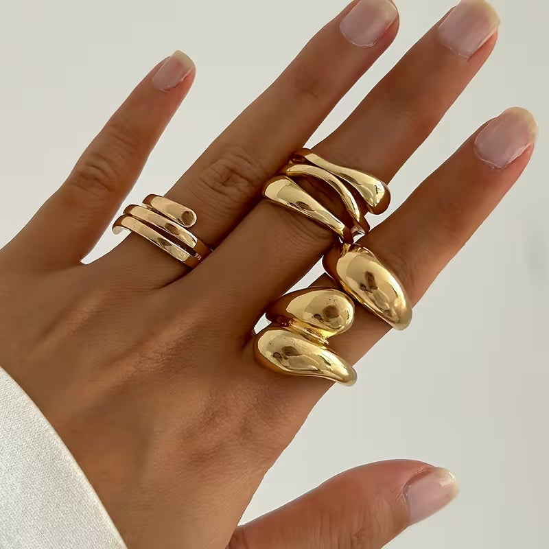 Hand wearing multiple gold rings on a neutral background