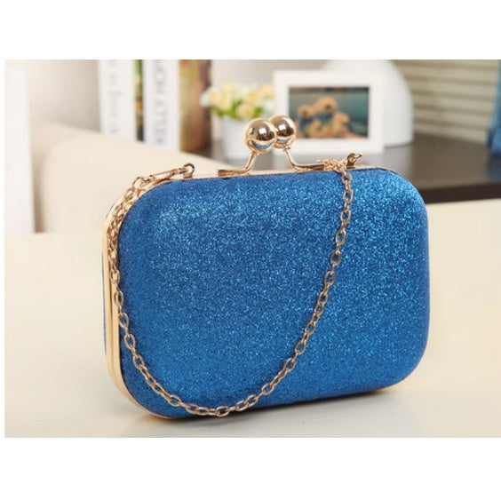 Blue glittery clutch bag with gold chain handle on a light surface.