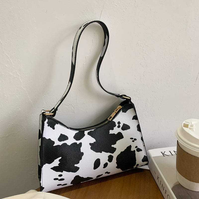 Black and white cow print handbag on a wooden surface with a light gray background