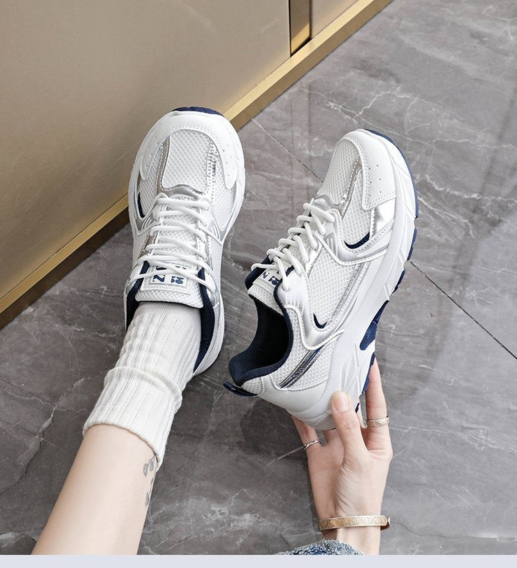 White sneakers with blue accents held by a person on a gray floor.