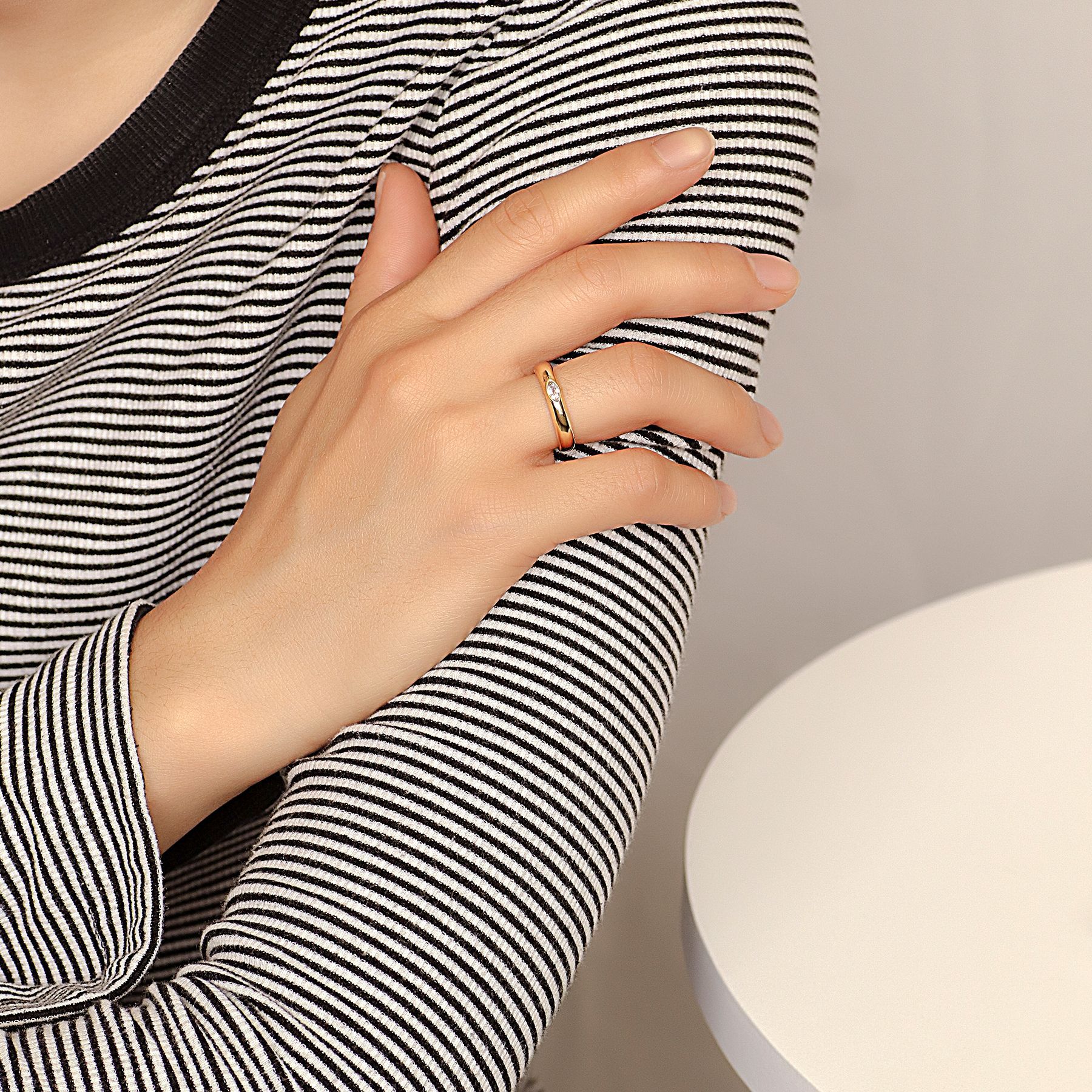 Hand wearing a gold ring with a diamond, against a neutral background