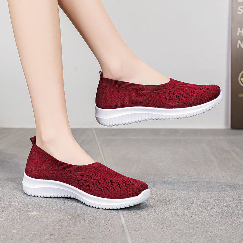 Red slip-on shoes with white soles worn by a person on a gray floor.