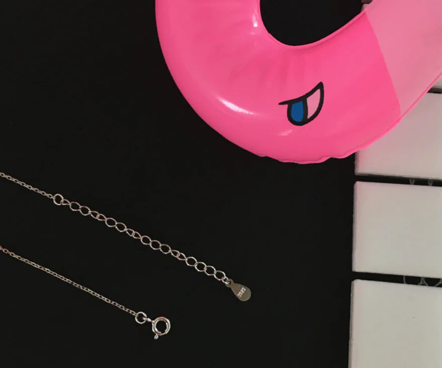 Silver necklace on a black surface with a pink inflatable ring in the background