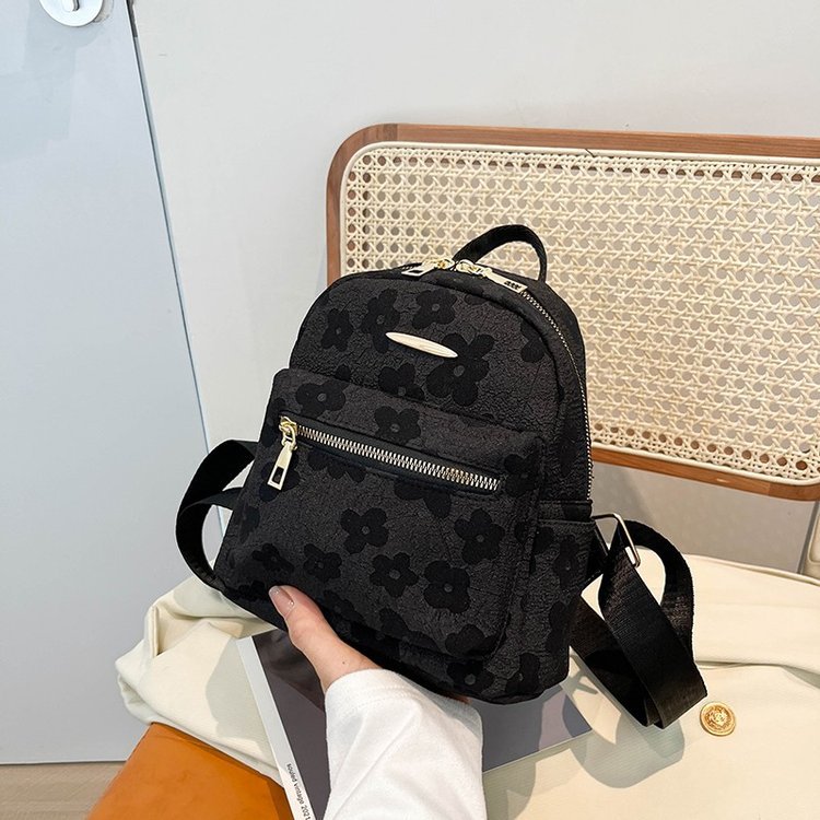 Black floral-patterned backpack held by a person with a light-colored background
