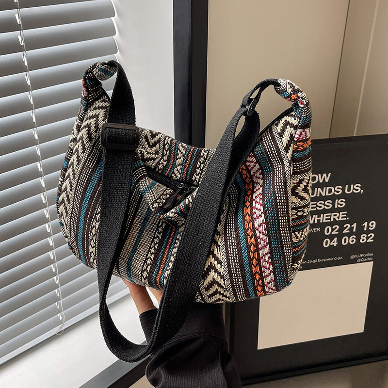 Multicolored patterned bag with black strap leaning against a wall.