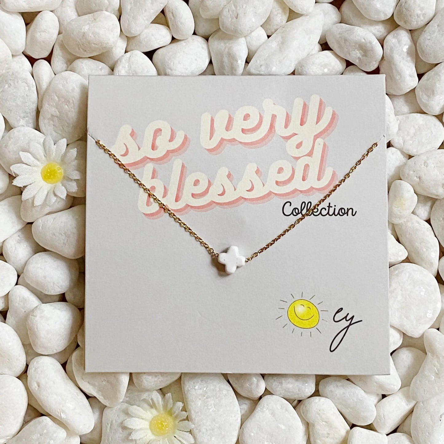 Necklace on a card with 'so very blessed' text, surrounded by pebbles and flowers.