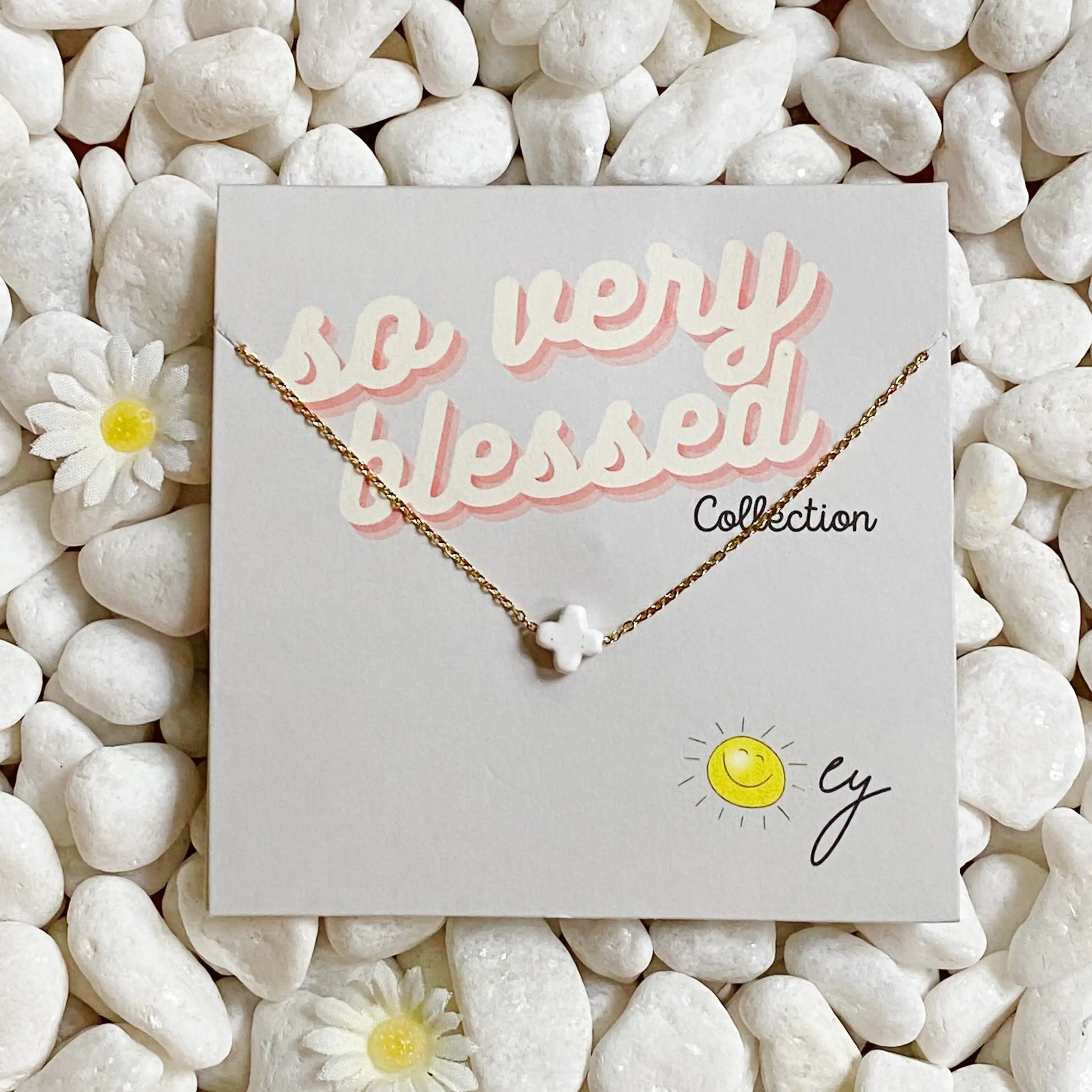 Necklace on a card with 'so very blessed' text, surrounded by pebbles and flowers.