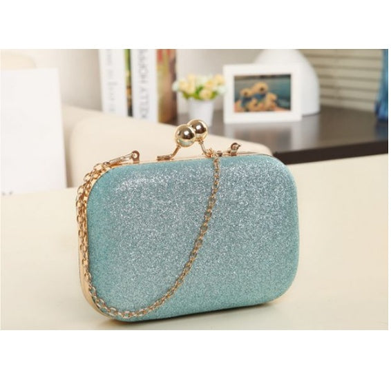 Light blue glittery clutch bag with gold chain on a light surface