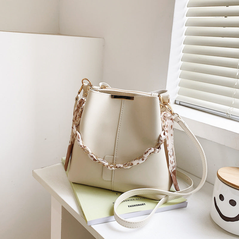 White handbag with a floral strap on a white surface next to a smiley face mug.