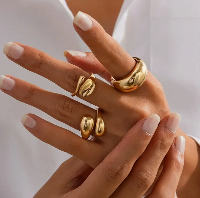Hand wearing three gold rings with a plain background