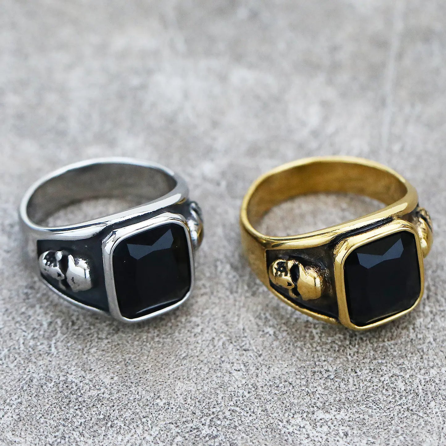 Two rings, one silver and one gold, with black stones on a textured surface.