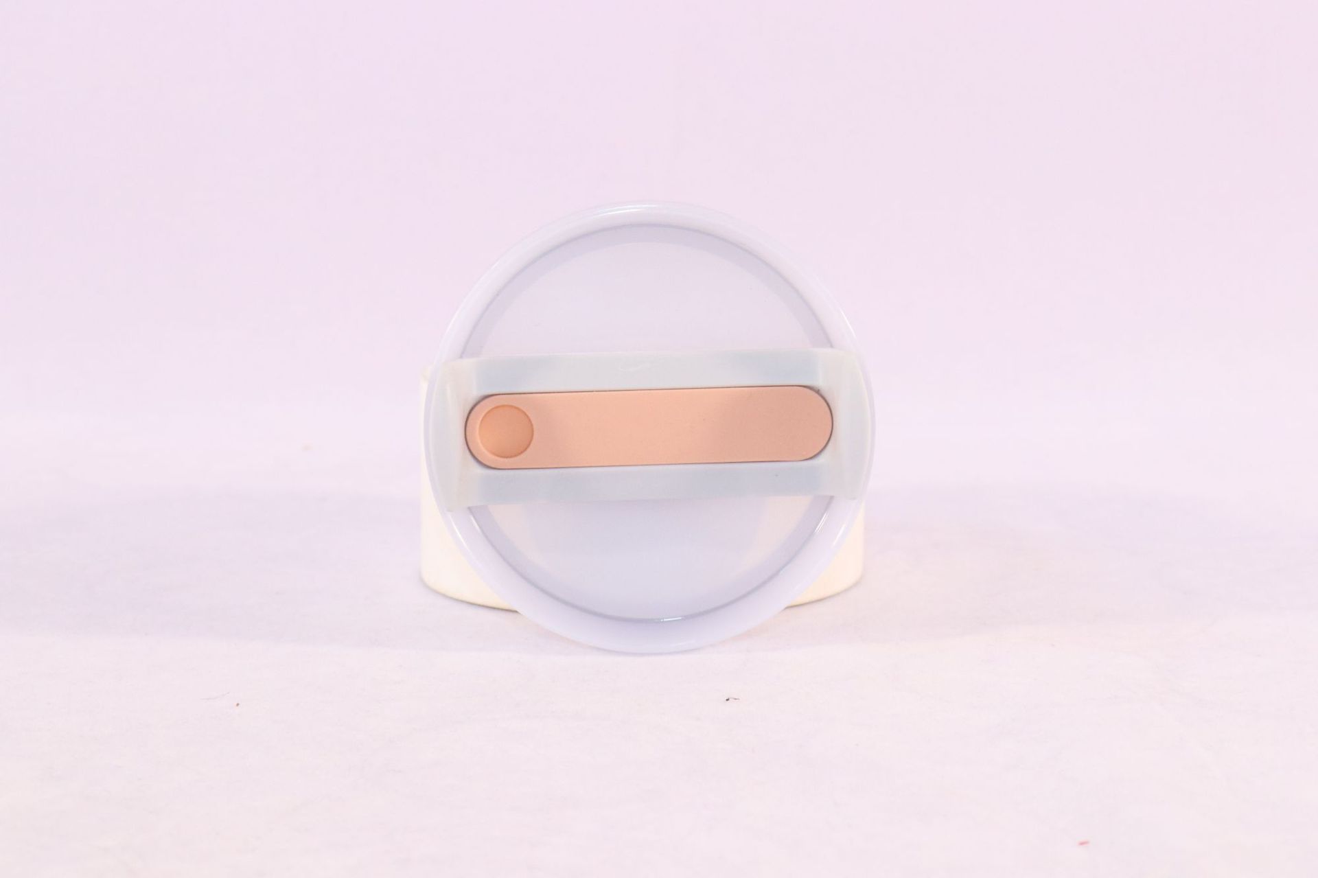 Clear container with a gold-colored object on a light purple background