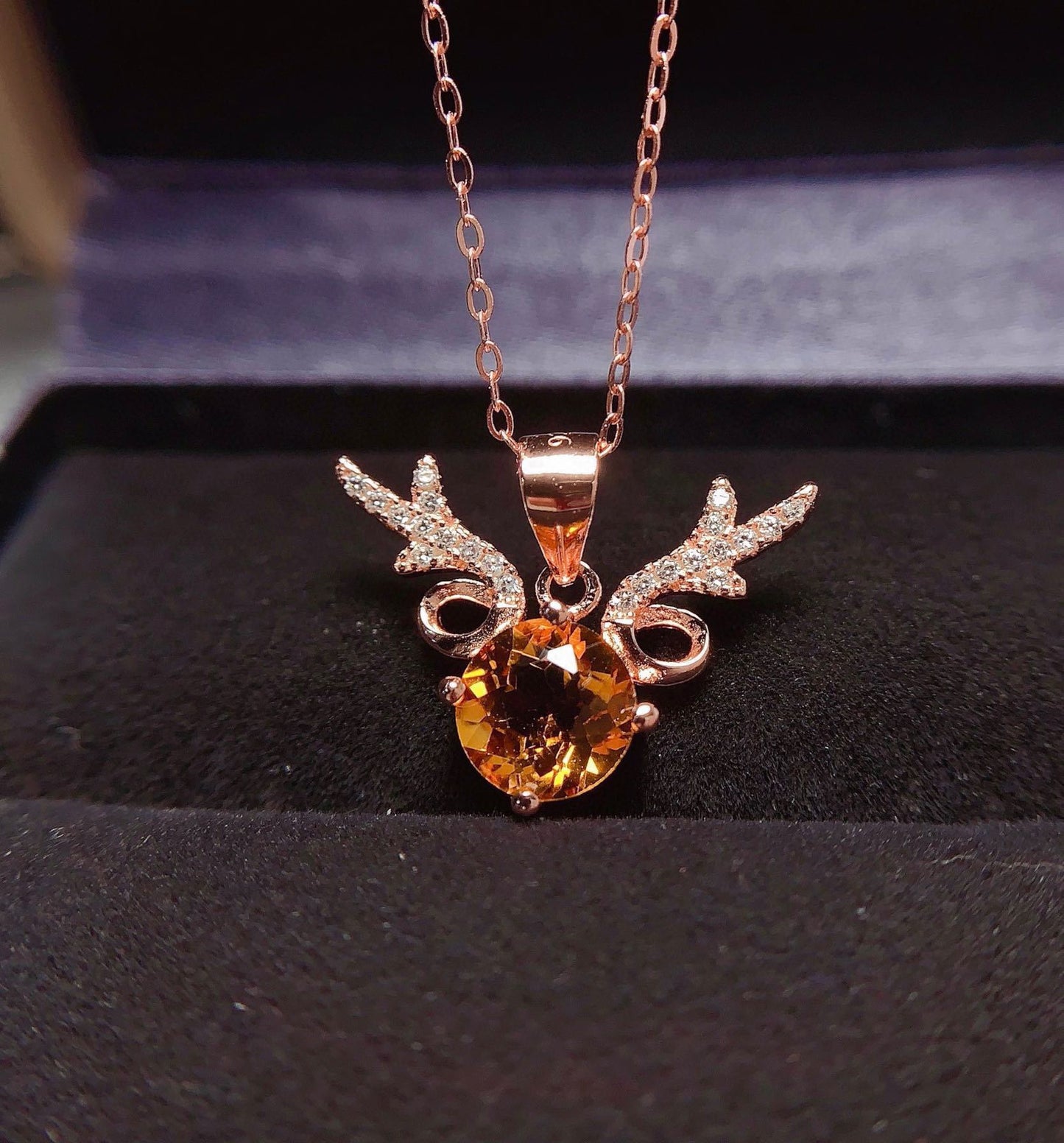 Rose gold necklace with a pendant featuring a large orange gemstone on a dark background