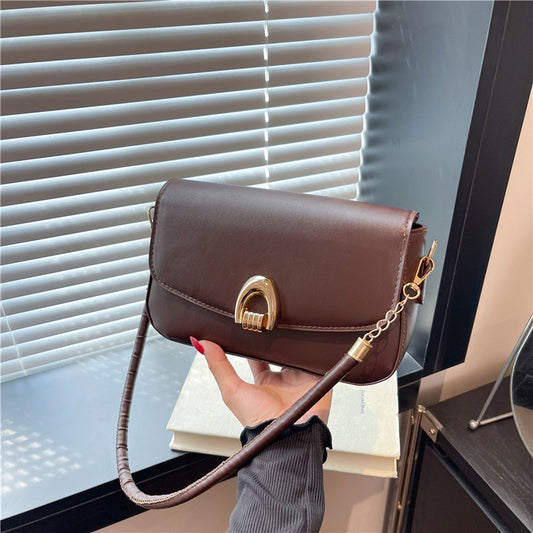 Brown handbag with gold clasp held by a hand in front of a window.
