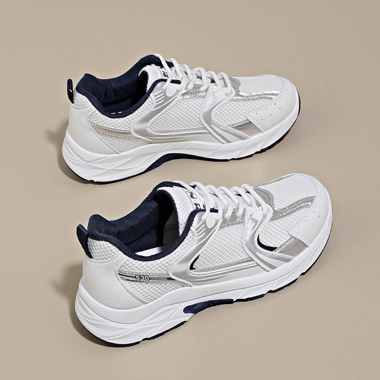 Pair of white running shoes with navy accents on a beige background