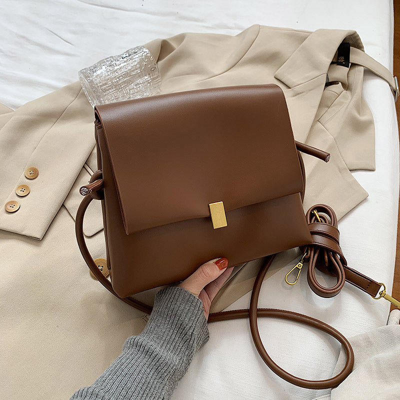 Brown leather handbag with gold clasp on a beige coat with buttons.