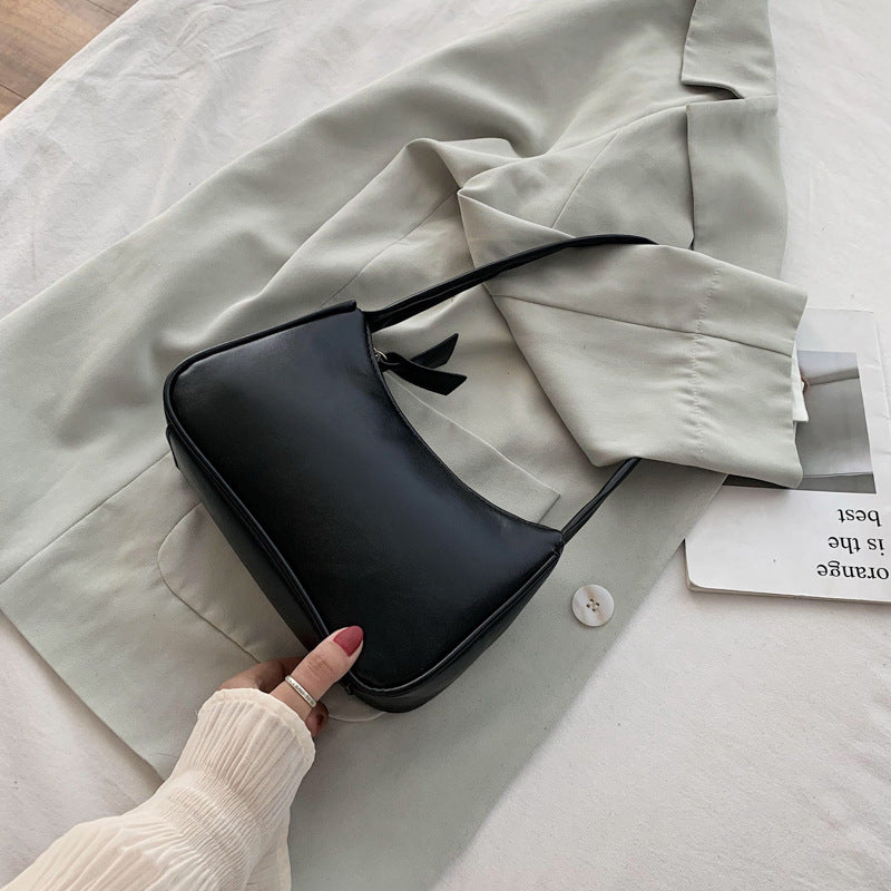 Black handbag with a bow detail on a light-colored fabric surface