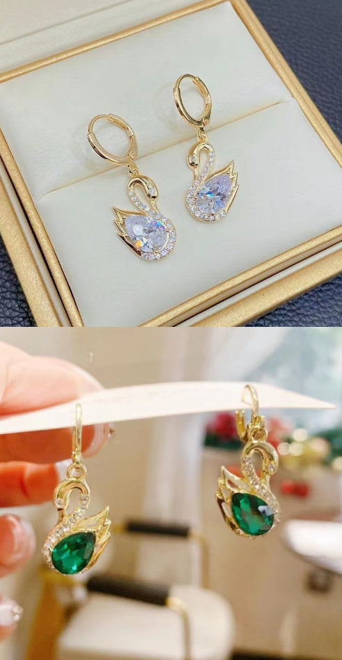 Gold earrings with green gemstones displayed in a box and held by a hand.