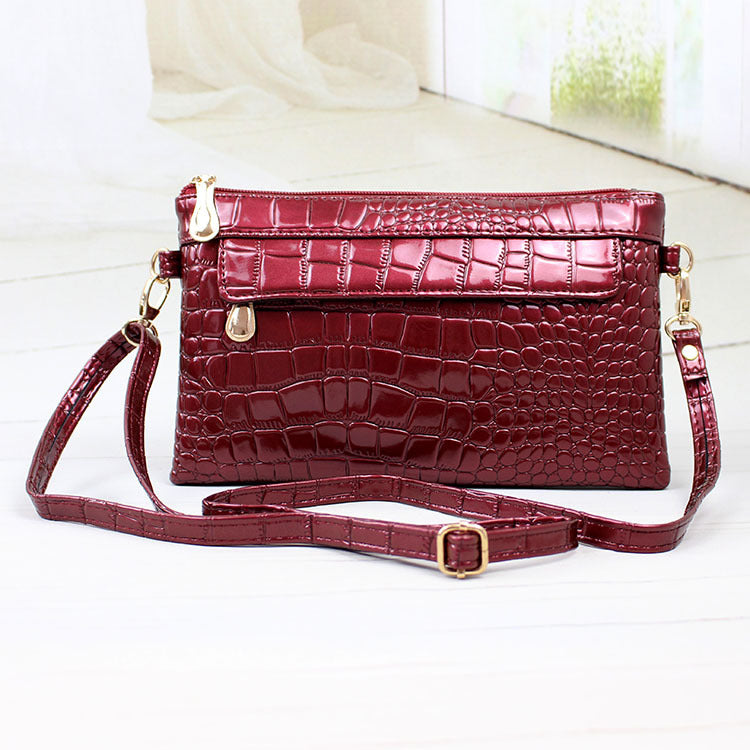 Red crocodile-patterned handbag with gold accents on a white background