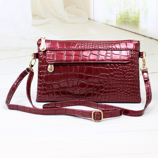 Red crocodile-patterned handbag with gold accents on a white background